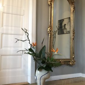 feireiss location Arrangement mit Strelitzien in moderner Keramikvase. Goldener neobarocker Spiegel.