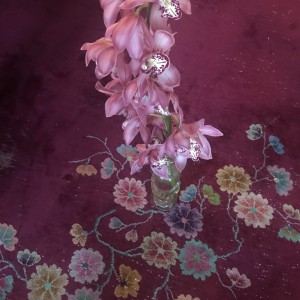 Morbide schön: Orchideen Stil mit großen Orchideenblüten in Glasvase auf rotem Teppich mit Blütenmuster.