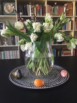 Foto/Styling: Nikolas Feireiss Weisse gefüllte Tulpen. Großer Strauß in runder Glasvase vor Bücherregal auf schwarz weiss gepunktetem Tablett.