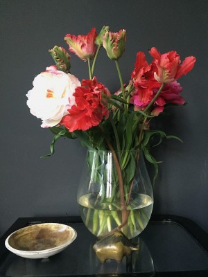 Foto/Styling: Nikolas Feireiss Rote Papageientulpen in runder Glasvase. vor schwarzem Hintergrund. Goldenes Keramikschale. Kleine Tierfigur.