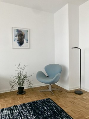 Blauer Stuhl i Stil der 60er Jahre. Grünpflanze, schwarz-grauer Teppich.